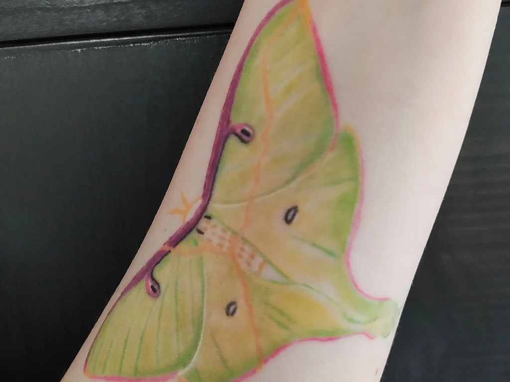 50 Animal Tattoo Ideas: The Complete Guide by Animal, Style and Placement 3 Colour luna moth tattoo in pale green and pink on a forearm