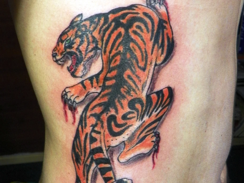 50 Animal Tattoo Ideas: The Complete Guide by Animal, Style and Placement 9 Japanese style tiger tattoo climbing down a person's ribs in red and black ink