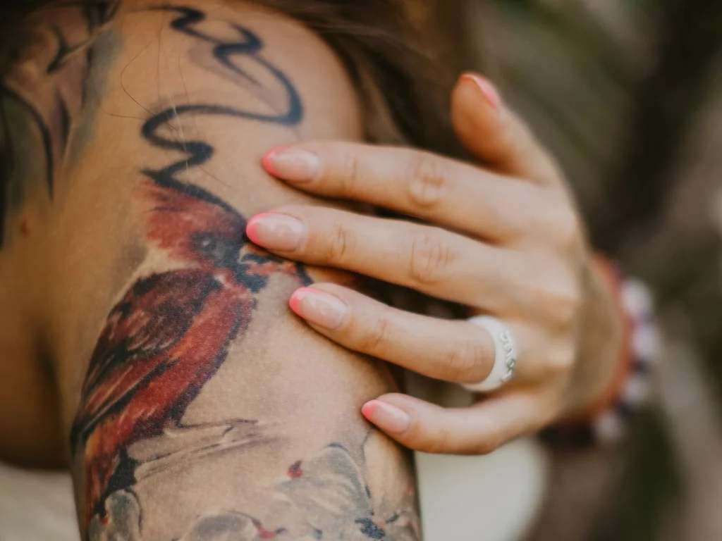 35 Bird Tattoo Ideas: Meanings, Species and Best Placements 7 Red bird tattoo with white blossom on an upper arm