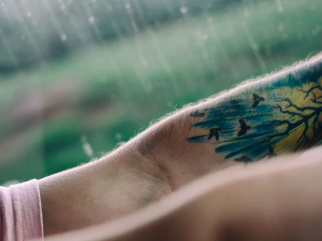 35 Bird Tattoo Ideas: Meanings, Species and Best Placements 9 Watercolour tattoo of birds flying out of a tree on a forearm