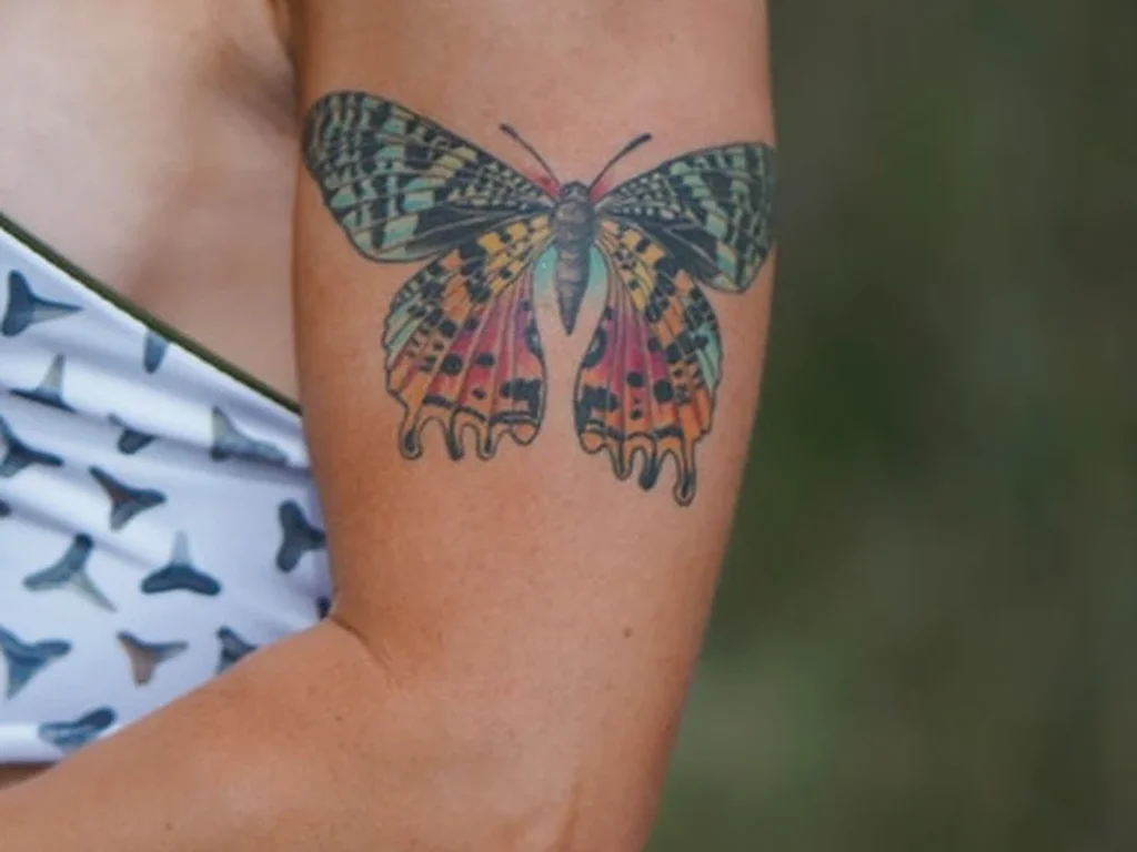 22 Butterfly Tattoo Ideas: Meanings, Styles and Best Placements 4 Colour butterfly tattoo with green and orange patterned wings on an upper arm