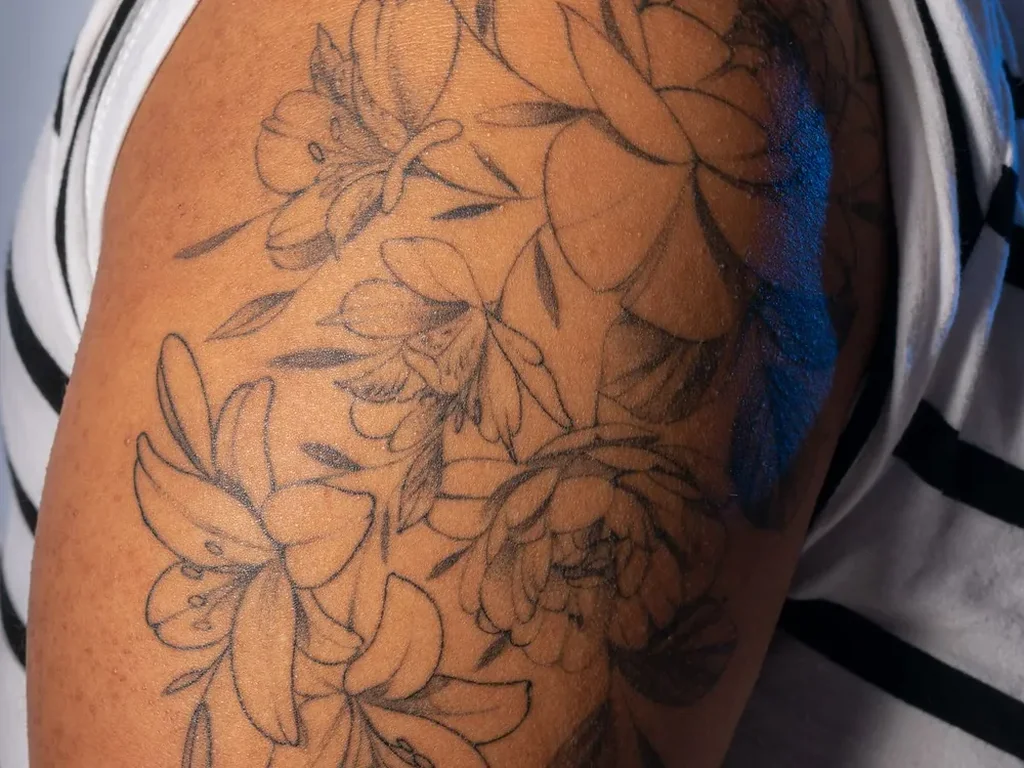 Fine line peony bouquet tattoo in black outline on an upper arm