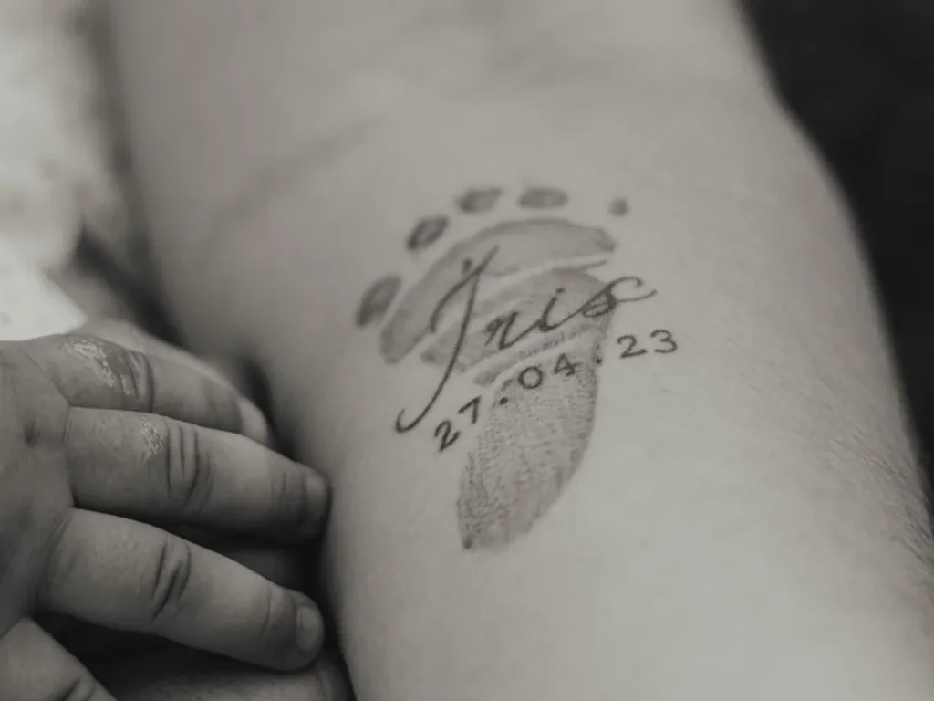 25 Fine Line Tattoo Ideas: Delicate Designs, Honestly Rated 16 Baby footprint tattoo with a name and birth date in fine script on a mother's forearm