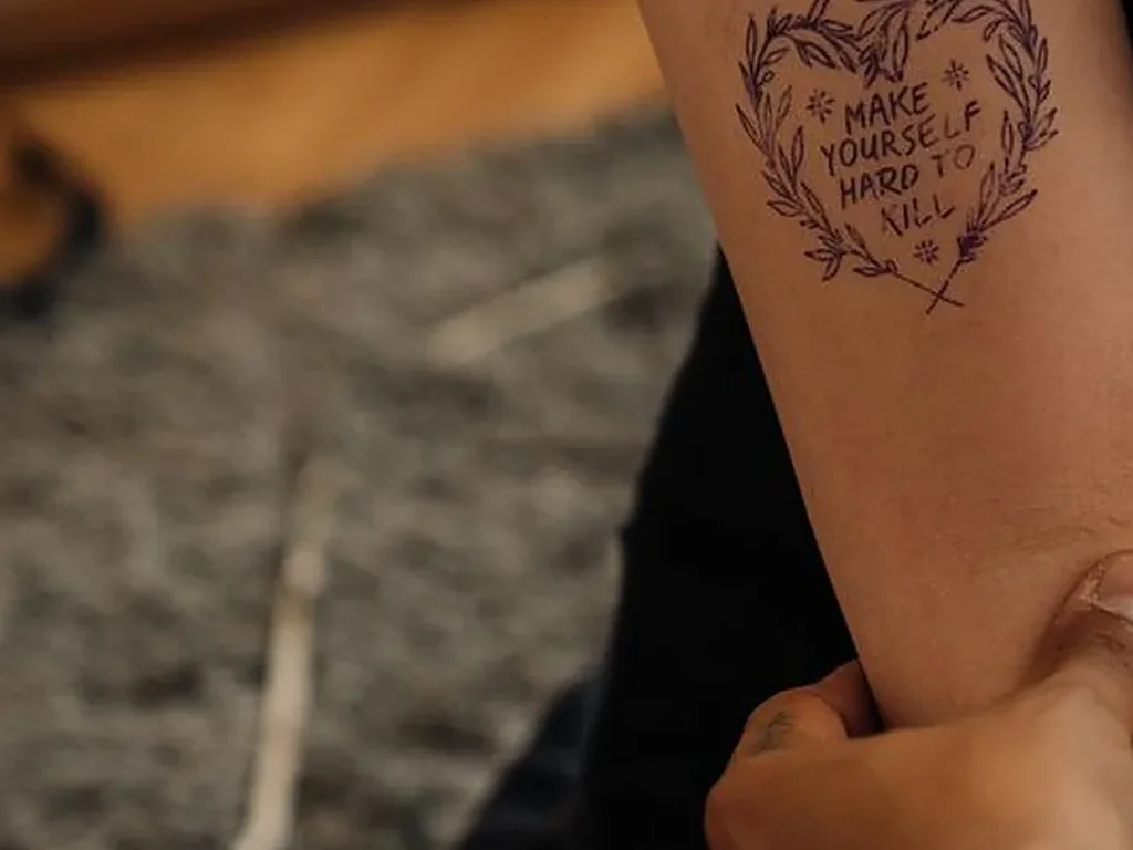 25 Fine Line Tattoo Ideas: Delicate Designs, Honestly Rated 18 Heart-shaped wreath tattoo with short words lettered inside, on a forearm