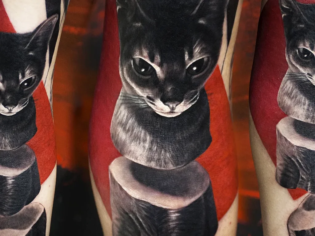 22 Pet Tattoo Ideas: Portraits, Paw Prints and Memorials Done Right 11 Graphic black cat tattoo with red geometric shapes photographed from three angles on legs