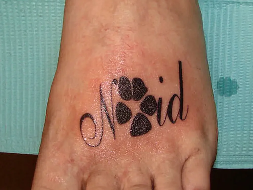22 Pet Tattoo Ideas: Portraits, Paw Prints and Memorials Done Right 18 Script name tattoo on a foot with a paw print worked into the lettering