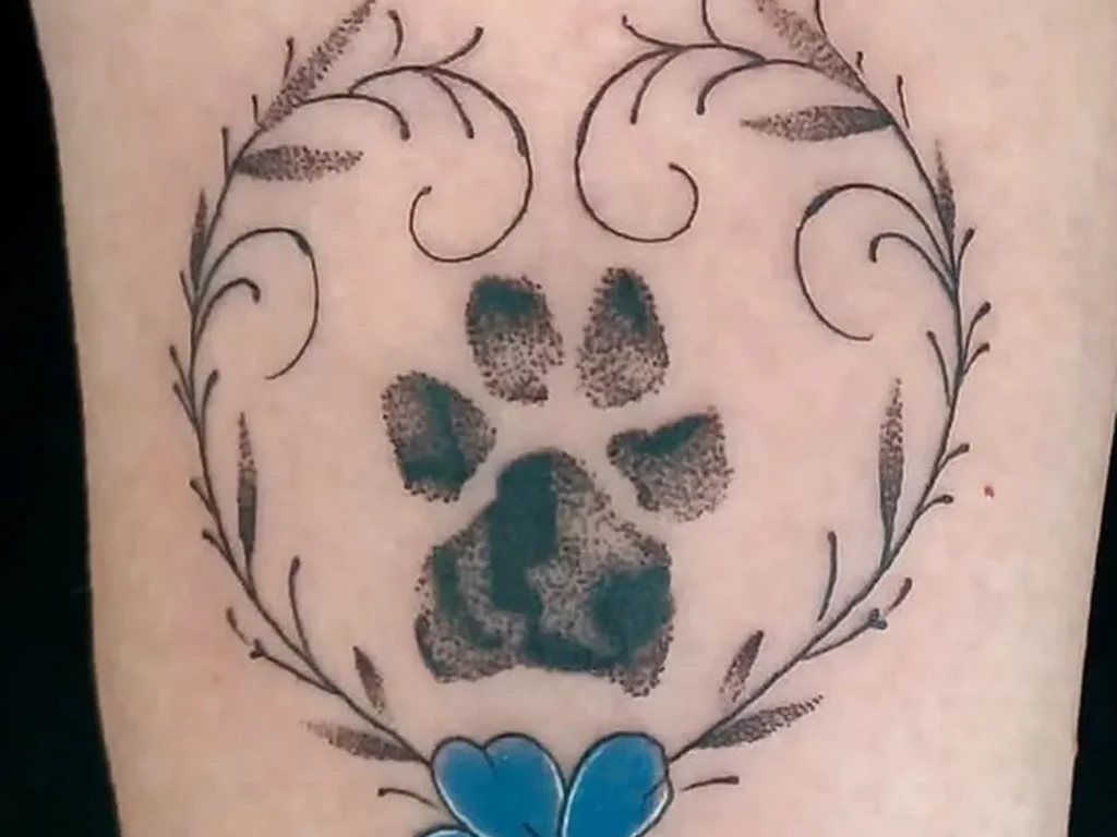 22 Pet Tattoo Ideas: Portraits, Paw Prints and Memorials Done Right 20 Real paw print tattoo framed by a laurel wreath with a blue flower on a forearm