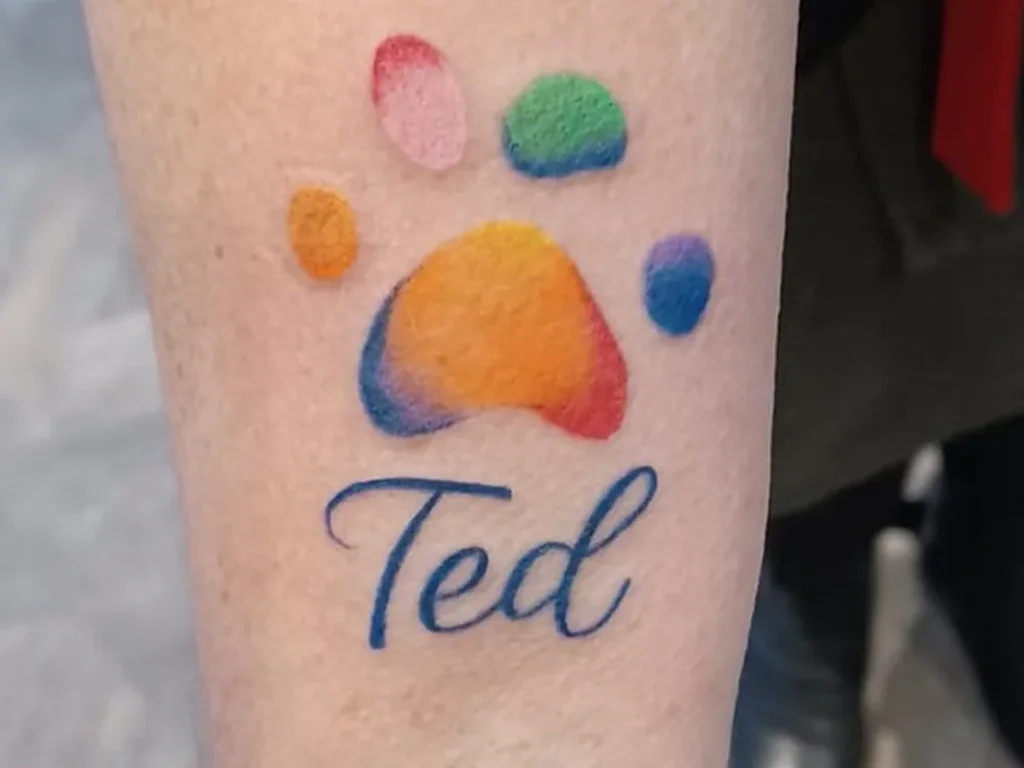 22 Pet Tattoo Ideas: Portraits, Paw Prints and Memorials Done Right 22 Rainbow watercolour paw print tattoo with the name Ted in script on a forearm