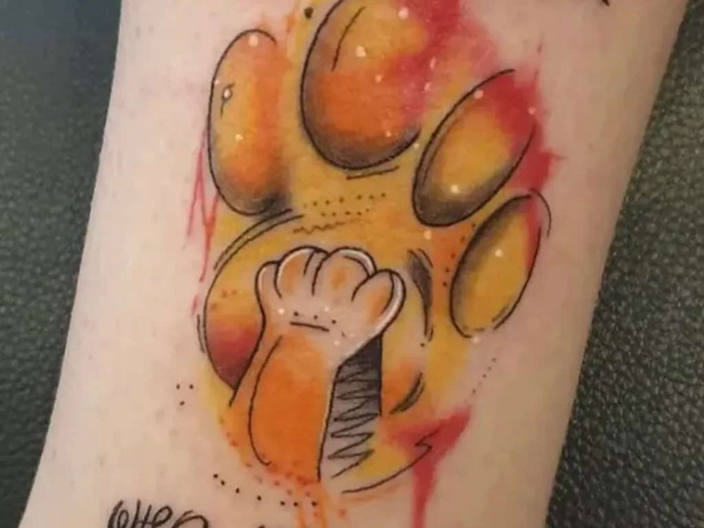 22 Pet Tattoo Ideas: Portraits, Paw Prints and Memorials Done Right 23 Orange watercolour paw print tattoo with a small cat silhouette and Remember Who You Are lettering on a lower leg