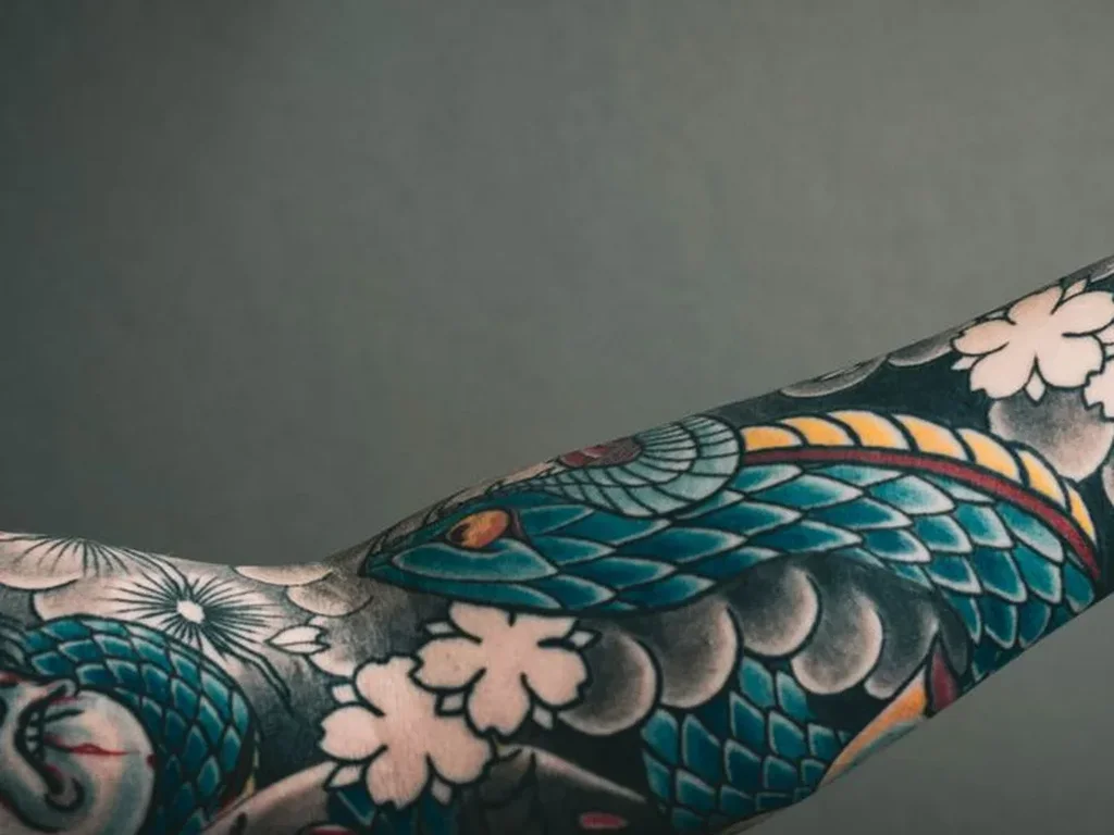 20 Snake Tattoo Ideas: Meanings, Styles and Placements That Work 4 Japanese hebi snake tattoo with teal scales and cherry blossoms on a forearm sleeve