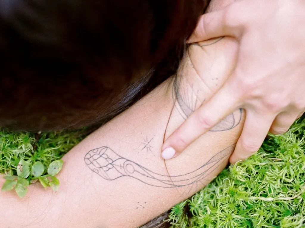 20 Snake Tattoo Ideas: Meanings, Styles and Placements That Work 15 Fine line snake tattoo in outline only on a forearm resting on grass