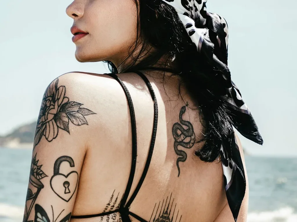 20 Snake Tattoo Ideas: Meanings, Styles and Placements That Work 18 Black coiled snake tattoo on a woman's shoulder blade at the beach